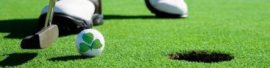 Golfer's feet on green with putter and golf ball with QA mark