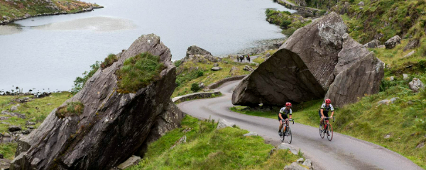 Two people cycling up a winding road and boulders jut out from the surround hillocks.